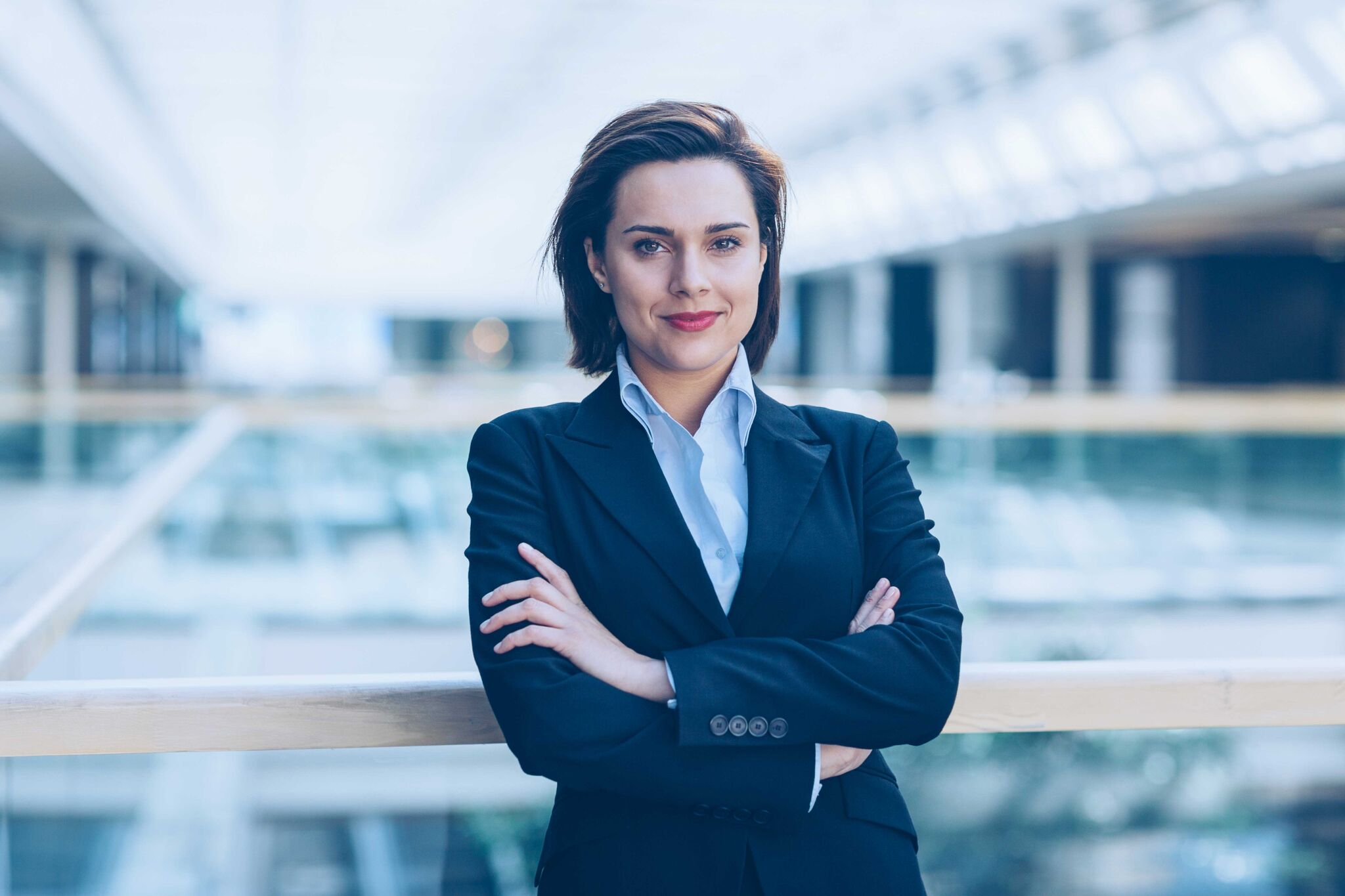Young woman in business wear standing with armes crossed in business environment, with copy space.