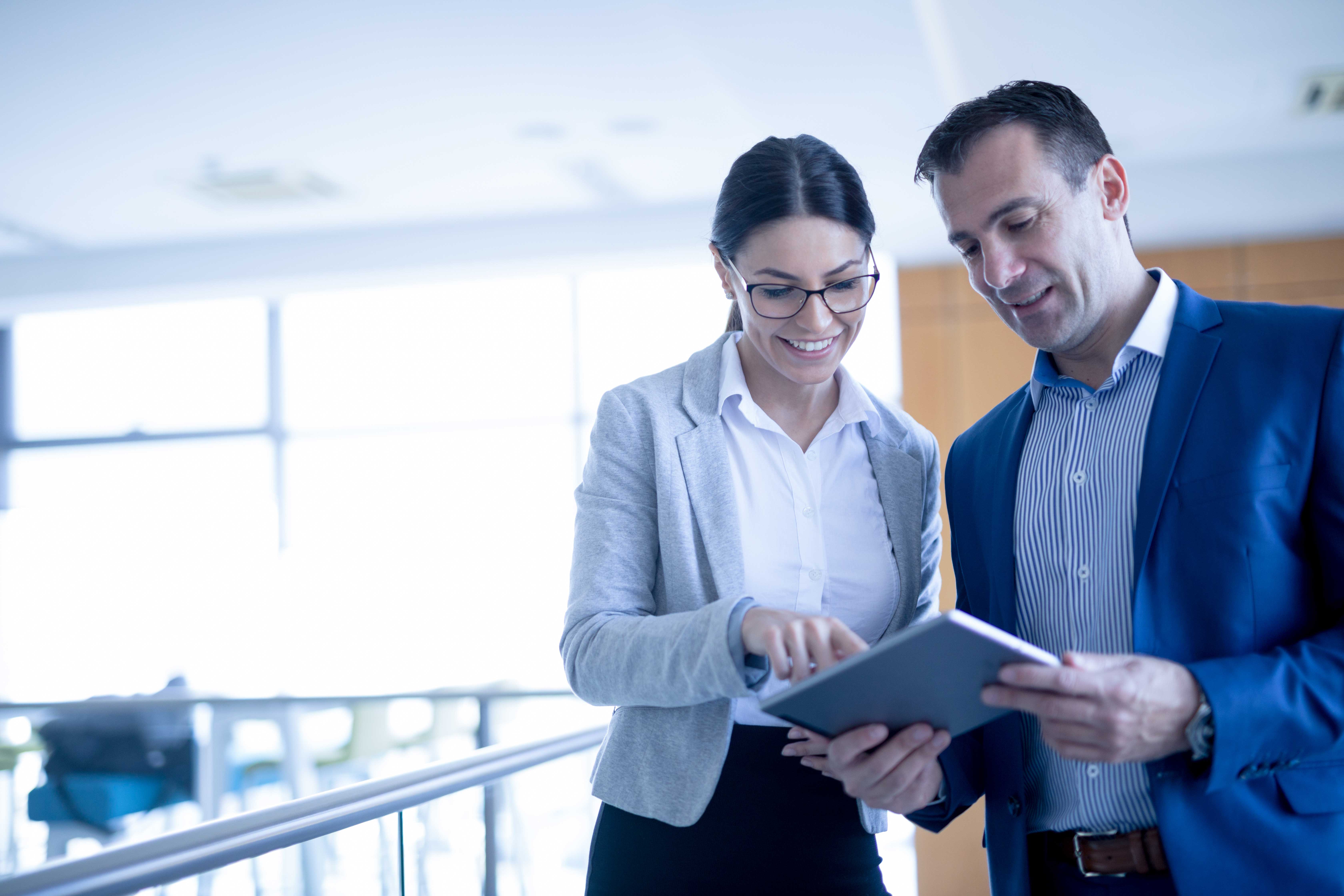 Accounts Payable Automation - Two mixed-age business people are discussing business strategy in the office building hallway using digital tablet. Front view. Copy space.